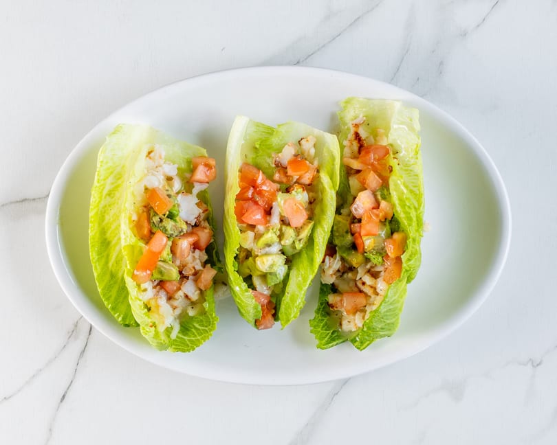 Three fresh lettuce wraps filled with shrimp, avocado, and tomato on a white plate.