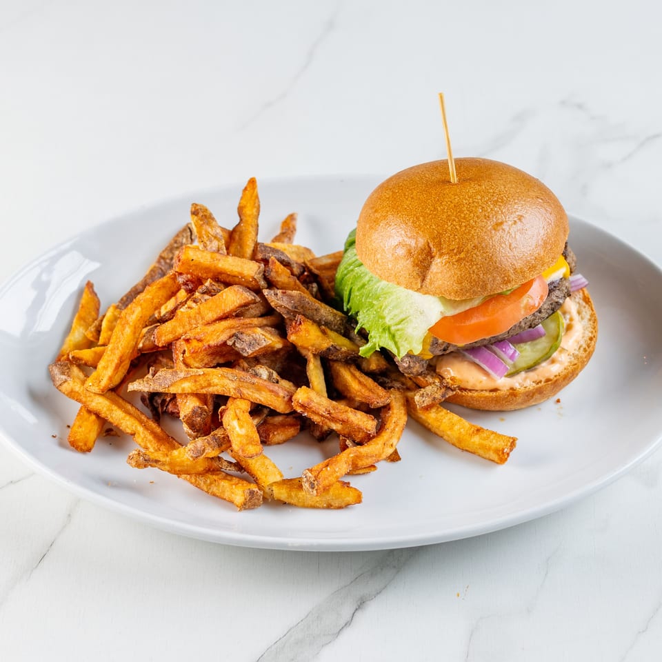 A cheeseburger with fresh vegetables and a side of golden-brown fries on a white plate.