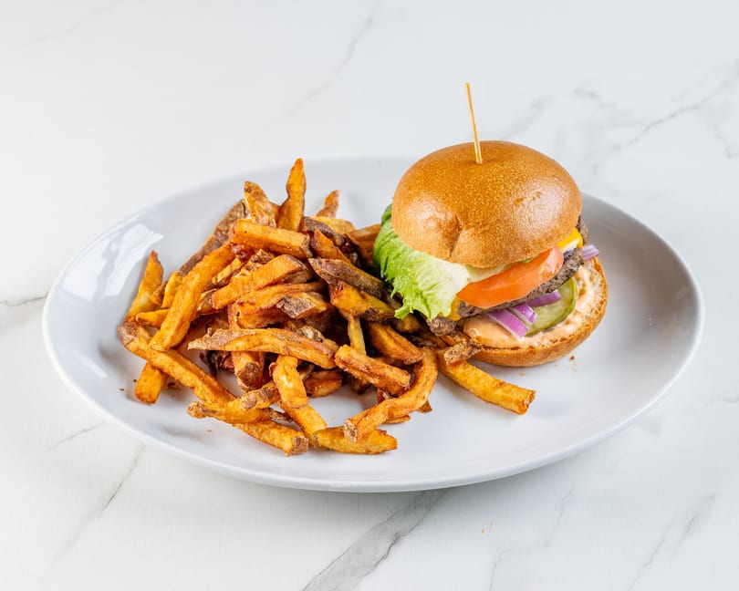 A cheeseburger with fresh vegetables and a side of golden-brown fries on a white plate.