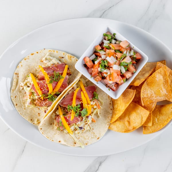 Two tuna tacos with mango and slaw, served with pico de gallo and tortilla chips on a white plate.