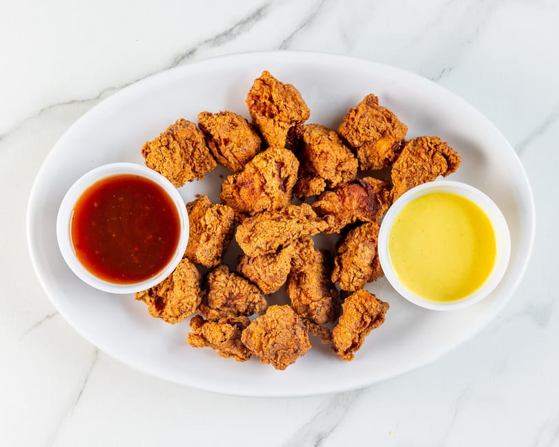 Crispy fried chicken pieces with sweet chili and honey mustard sauces on a white plate.