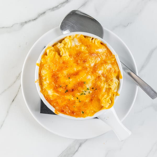 Golden-brown baked mac and cheese in a white serving dish with a spoon on a marble surface.
