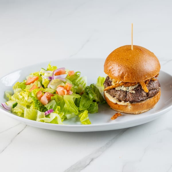 Burger with blue cheese, crispy onions, and a side salad on a white plate.