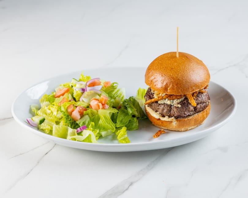 Burger with blue cheese, crispy onions, and a side salad on a white plate.