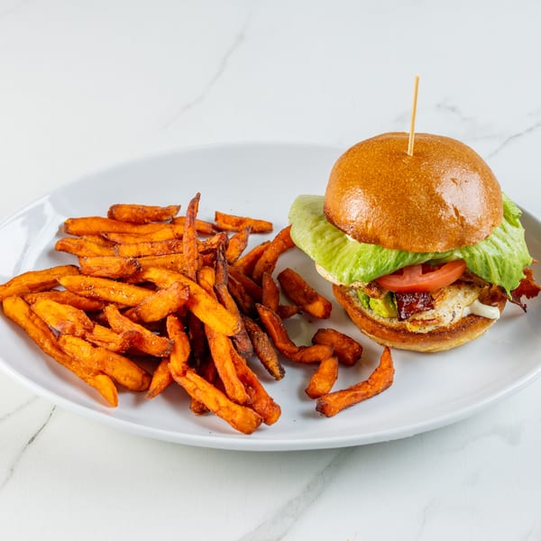 Chicken sandwich with bacon, avocado, tomato, and lettuce, served with sweet potato fries.