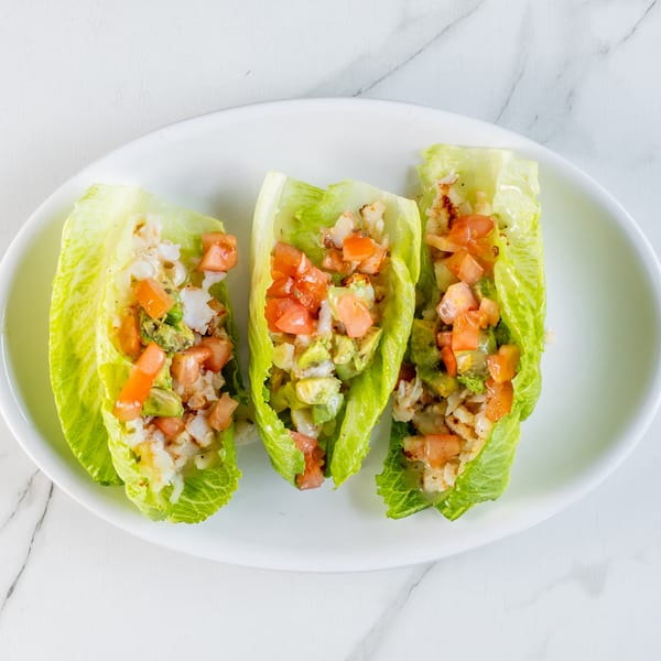 Three lettuce wraps filled with shrimp, diced tomatoes, and avocado on a white plate.