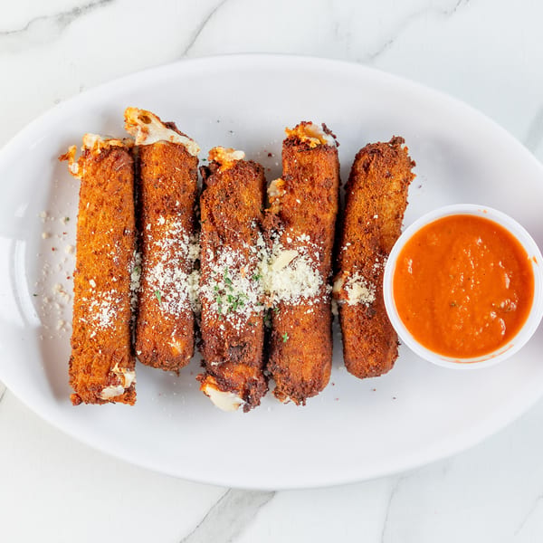 Golden-brown mozzarella sticks with melted cheese, Parmesan, and parsley, served with marinara sauce on a white plate.