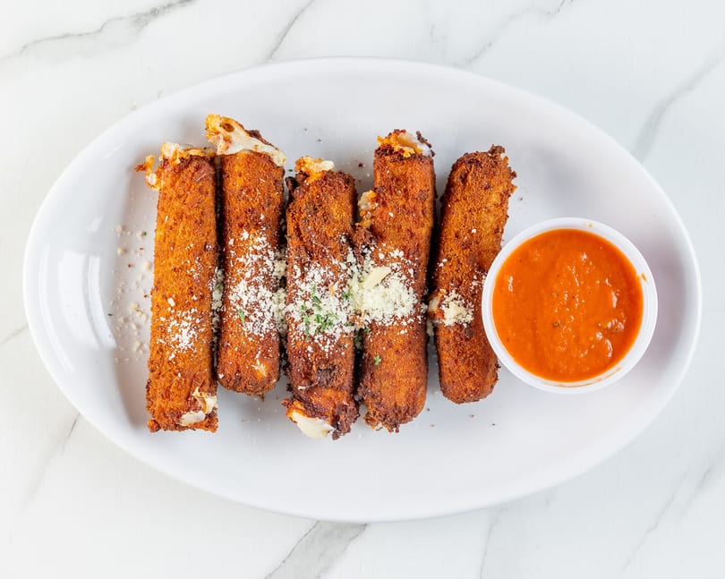 Golden-brown mozzarella sticks with melted cheese, Parmesan, and parsley, served with marinara sauce on a white plate.