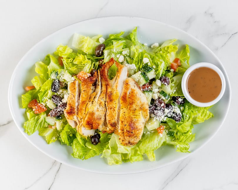 Grilled chicken salad with lettuce, olives, cucumbers, tomatoes, feta, and dressing.