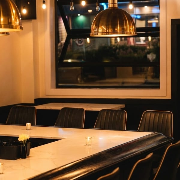 A dimly lit restaurant bar with a white marble counter, dark chairs, and golden pendant lights.