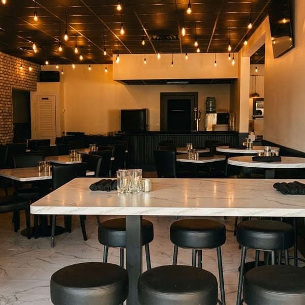 Modern restaurant interior with marble tables, black chairs, brick walls, and warm hanging lights.